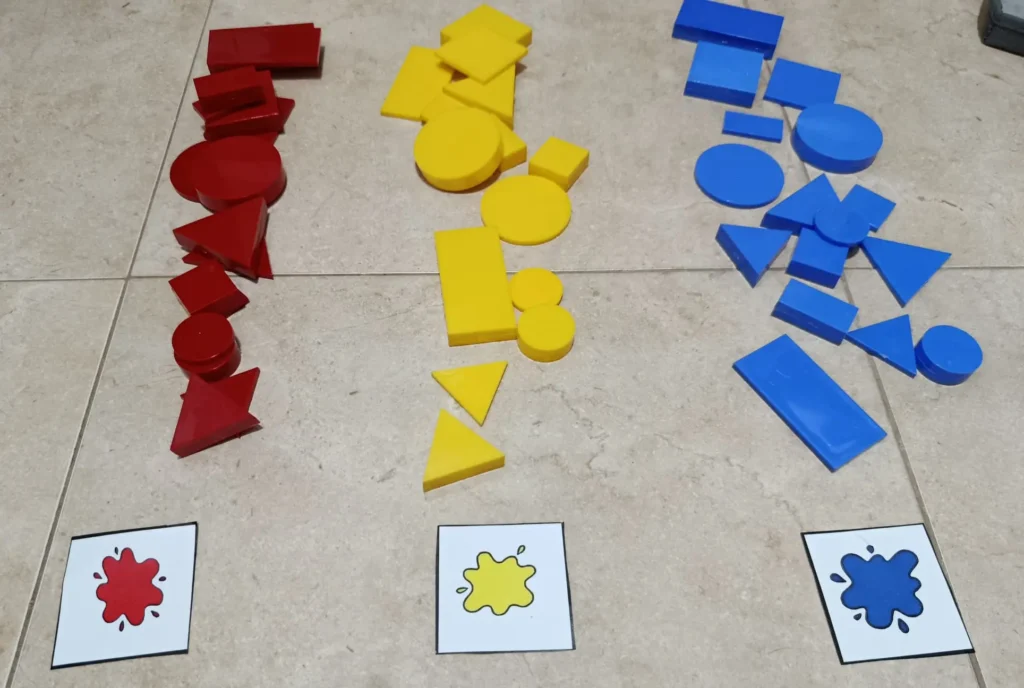 Juego de ordenación de bloques lógicos en el que organizamos las piezas en función de su color (rojo, amarillo y azul) separándolas con cartulinas indicadoras de color