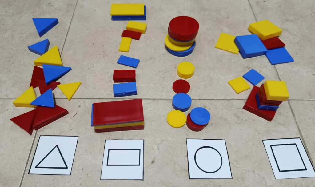 Juego de ordenación de bloques lógicos en el que organizamos las piezas en función de su forma (triángulo, rectángulo, círculo y cuadrado)) separándolas con cartulinas indicadoras de forma